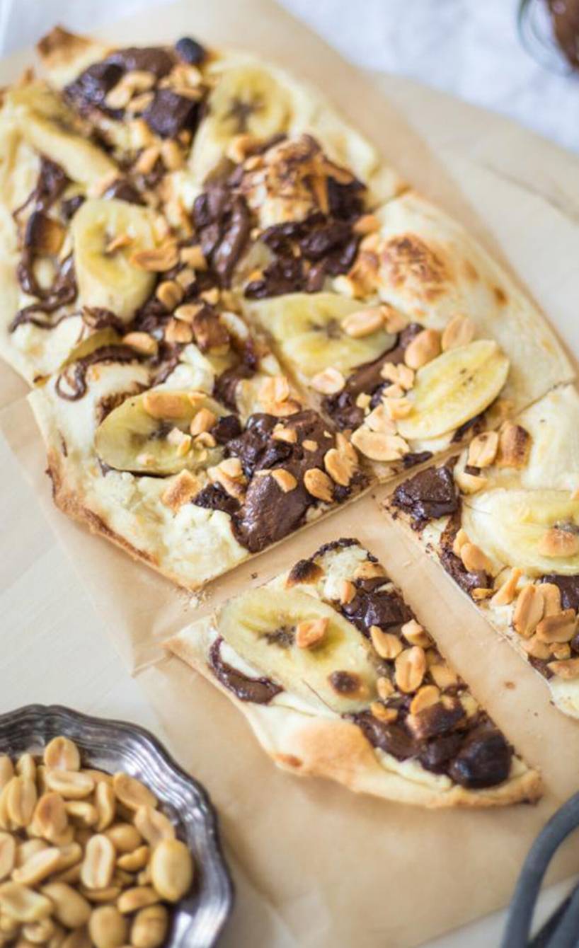 Schoko-Bananen-Flammkuchen angeschnitten auf einem Backblech getoppt mit Erdnusskernen
