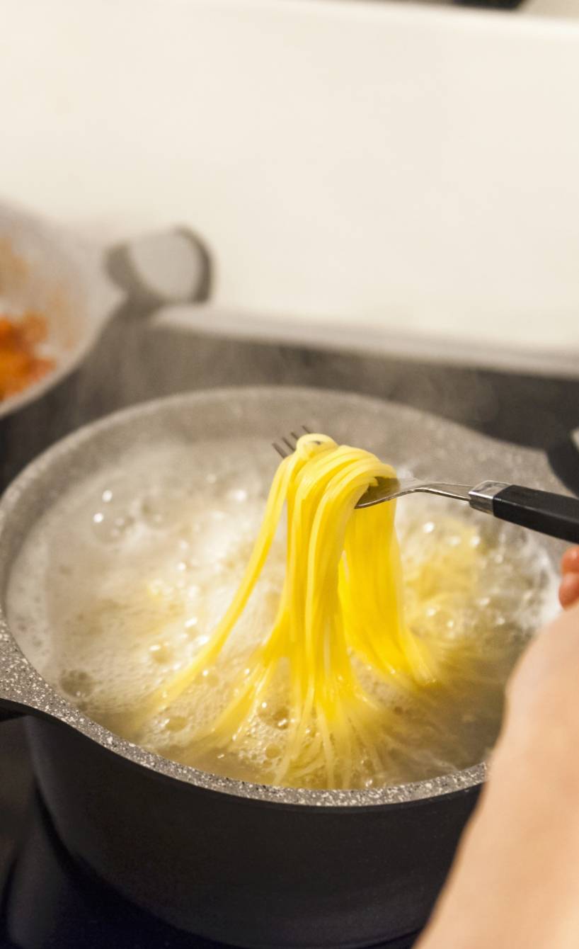 Frau schaut nach Spaghetti, die in Salzwasser kochen