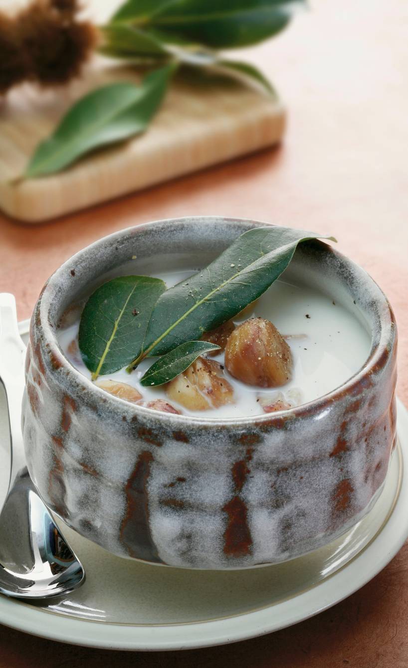 Maronensuppe in einer handgeformten Suppenschale auf einem Holztisch, daneben Maronen