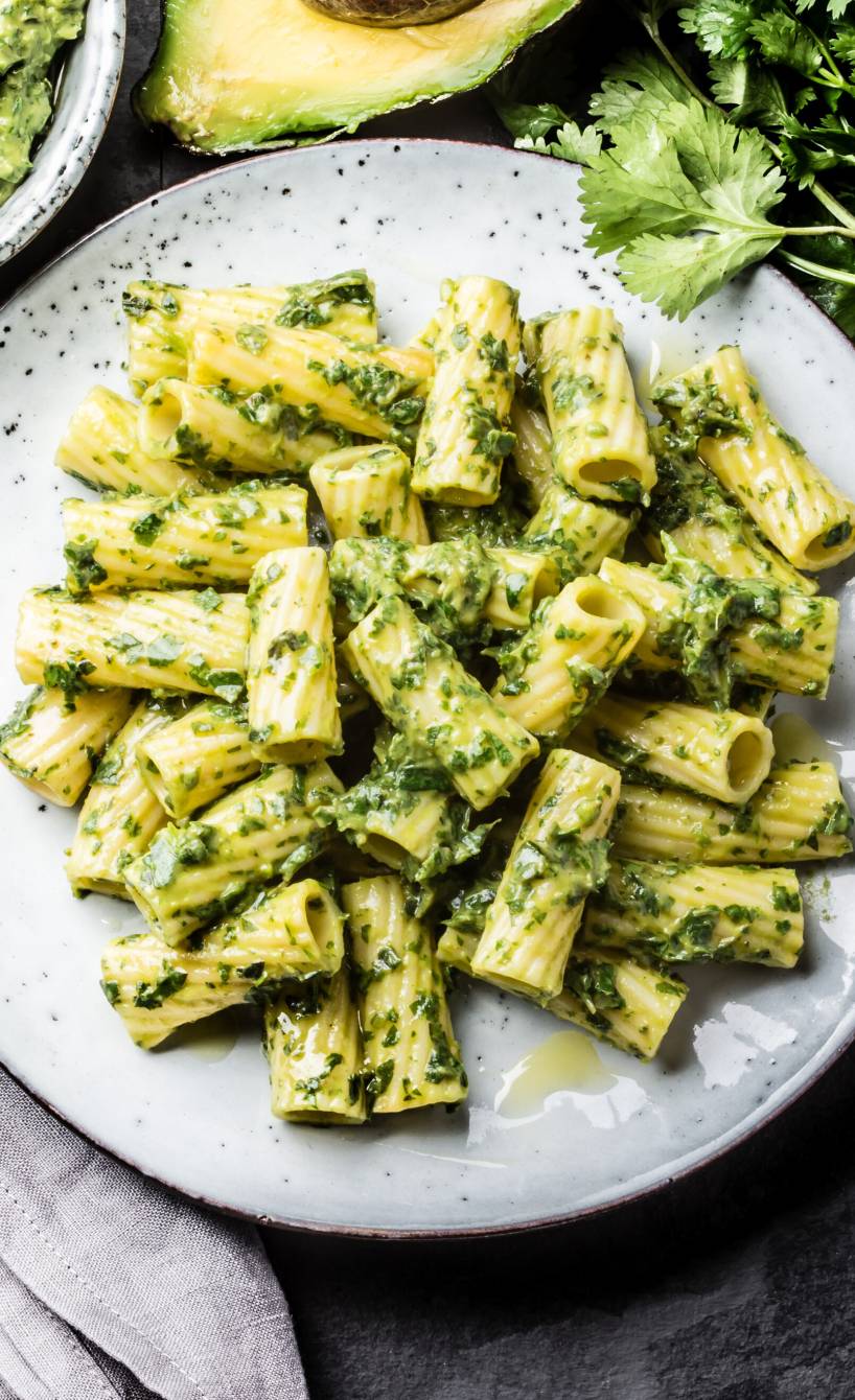 Avocado Pasta auf einem Teller, daneben eine halbierte Avocado