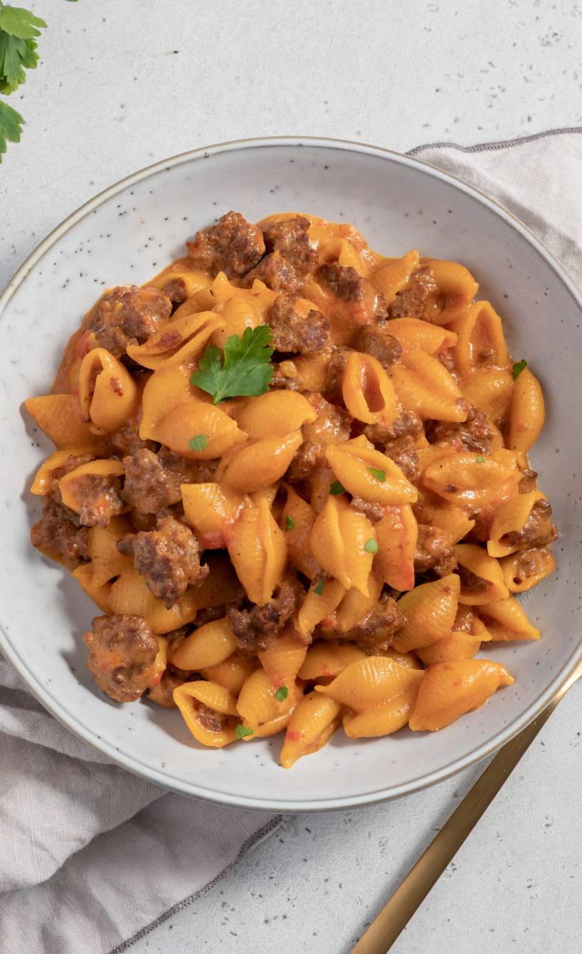 Cheeseburger Pasta in einem tiefen Teller, daneben frische Kräuter