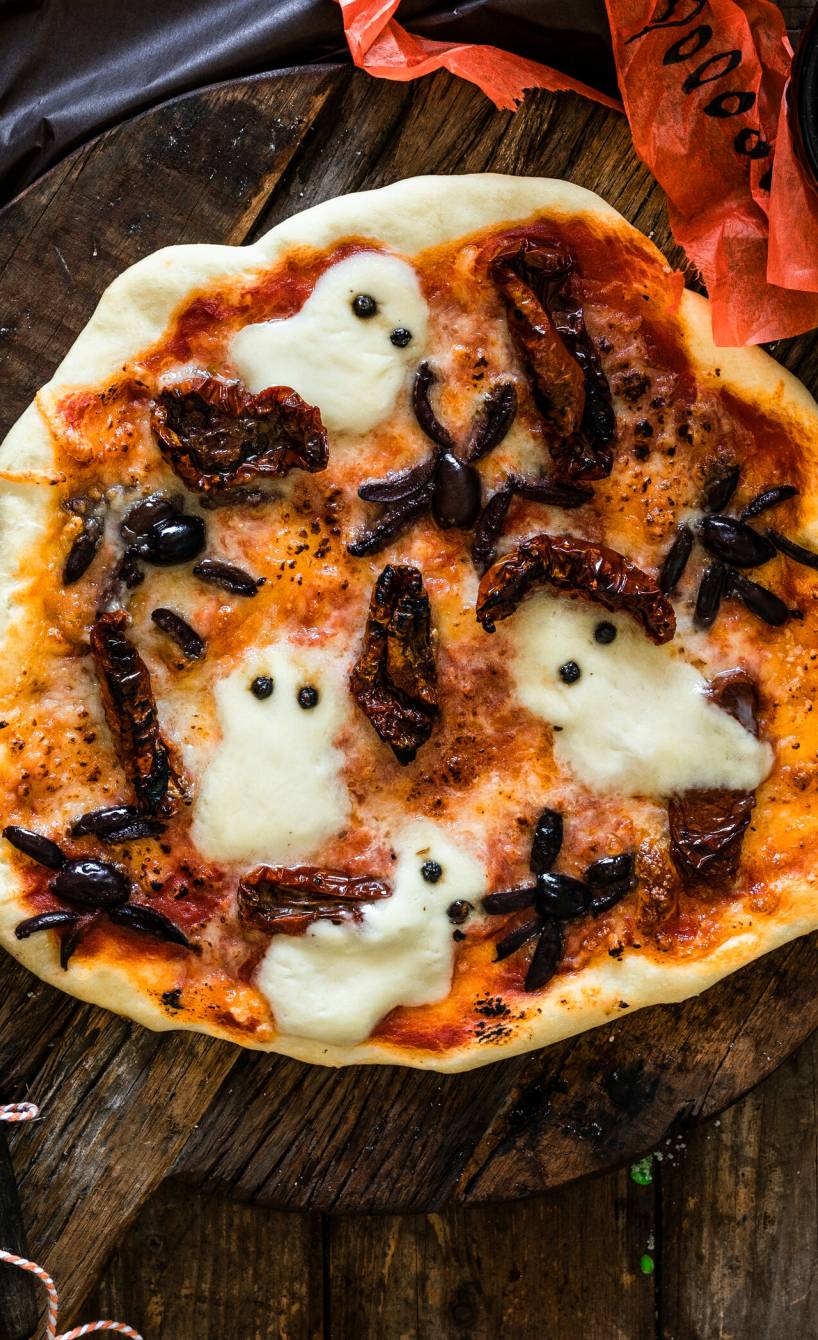Halloween-Pizza mit Mozzarella-Geistern im Ganzen auf einem Holztisch
