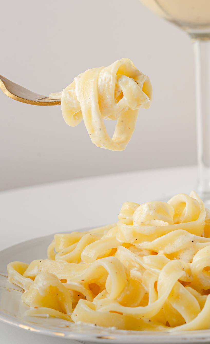 Bandnudeln mit Käsesoße aufgedreht auf einer Gabel über einem Teller mit Käsepasta