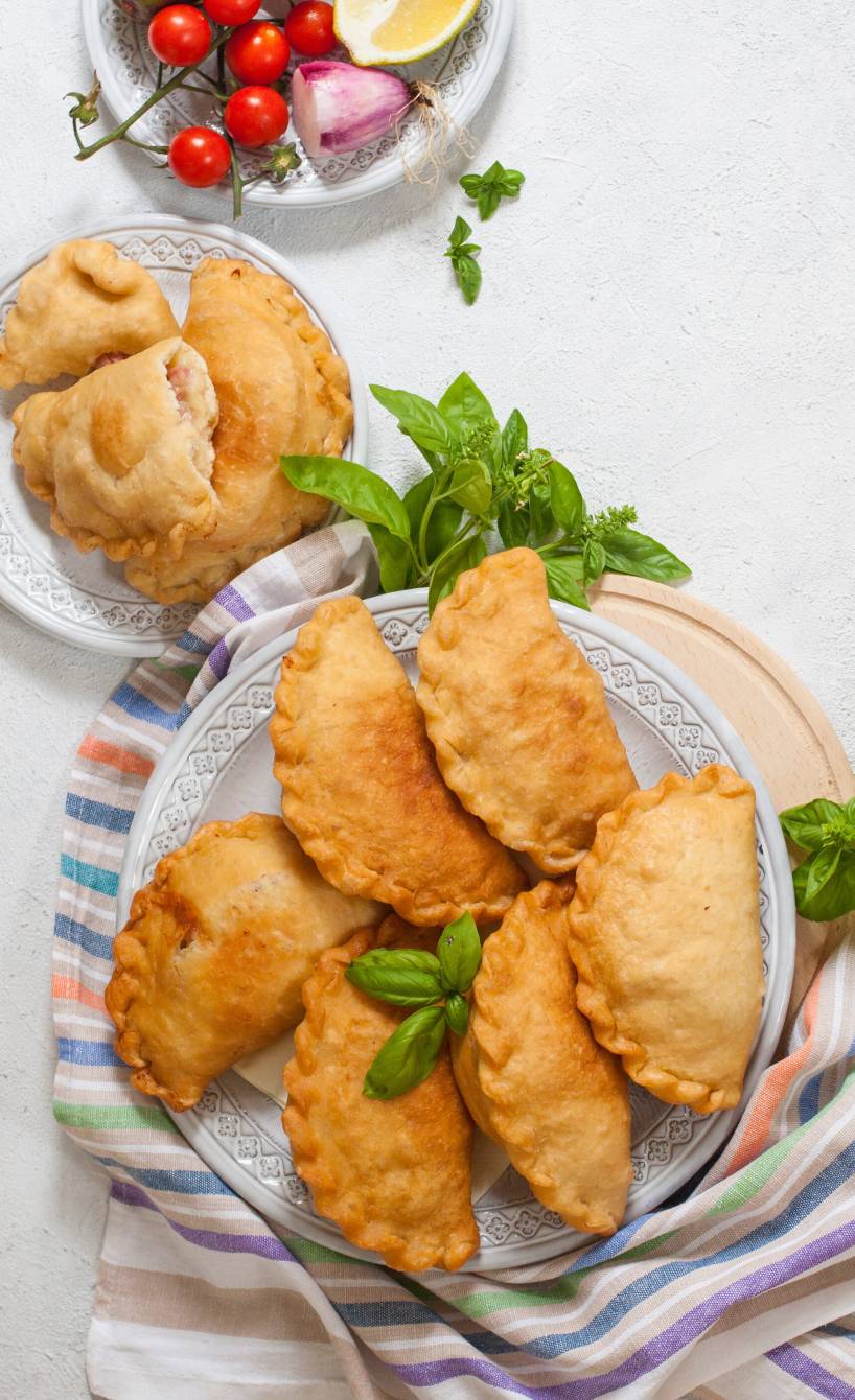 Panzerotti, gefüllte Teigtaschen auf zwei Tellern, einige aufgebrochen, sodass geschmolzener Mozzarella zu sehen ist