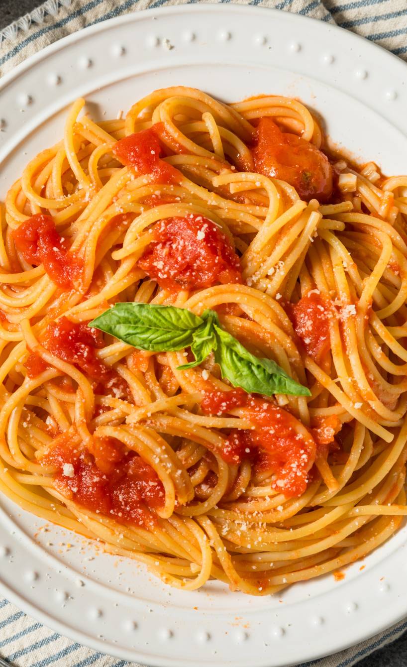 Spaghetti al pomodoro angerichtet auf einem weißen runden Teller garniert mit frischem Basilikum