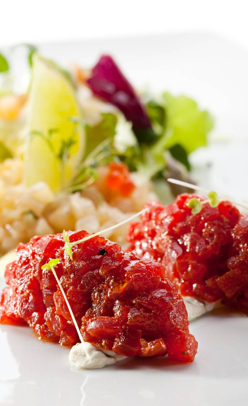 Rinder-Tartar in zwei Klecksen angeordnet auf einem Teller, dahinter Salat