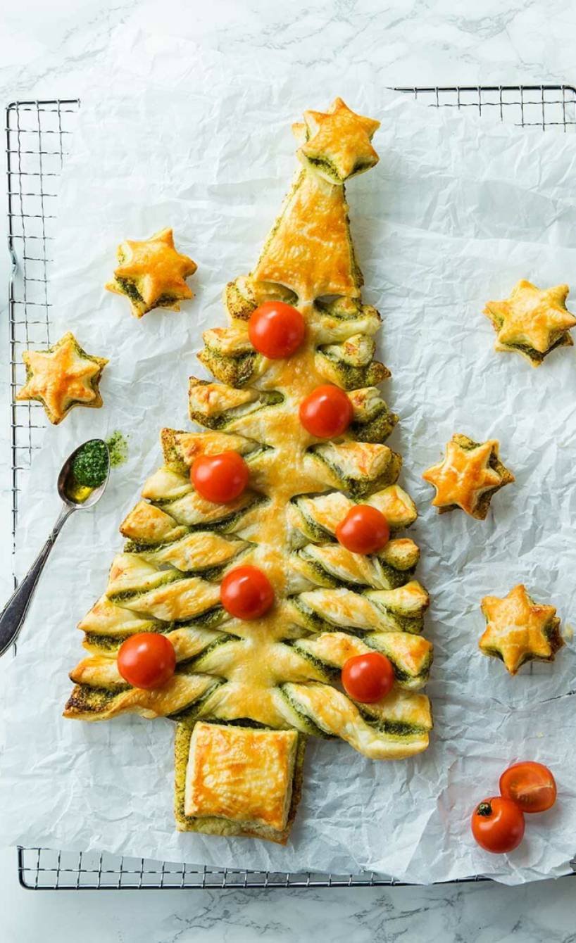 Tannenbaum aus Blätterteig auf einem Kuchengitter, daneben Kirschtomaten, grünes Pesto und Basilikum
