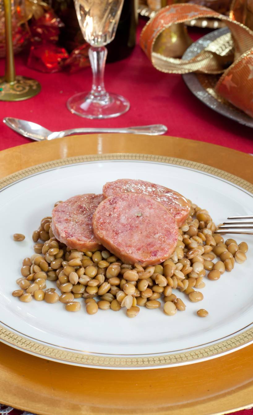 Cotechino e Lenticchie auf einem goldenen Teller angerichtet auf einem Tisch mit Silvesterdeko