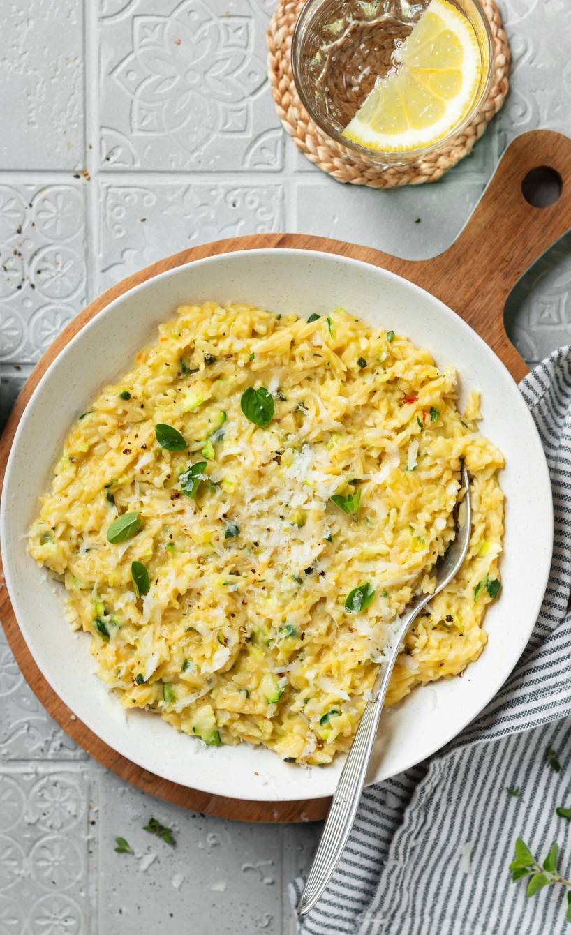 Orzotto in einem weißen Teller, daneben Parmesan und frischer Basilikum