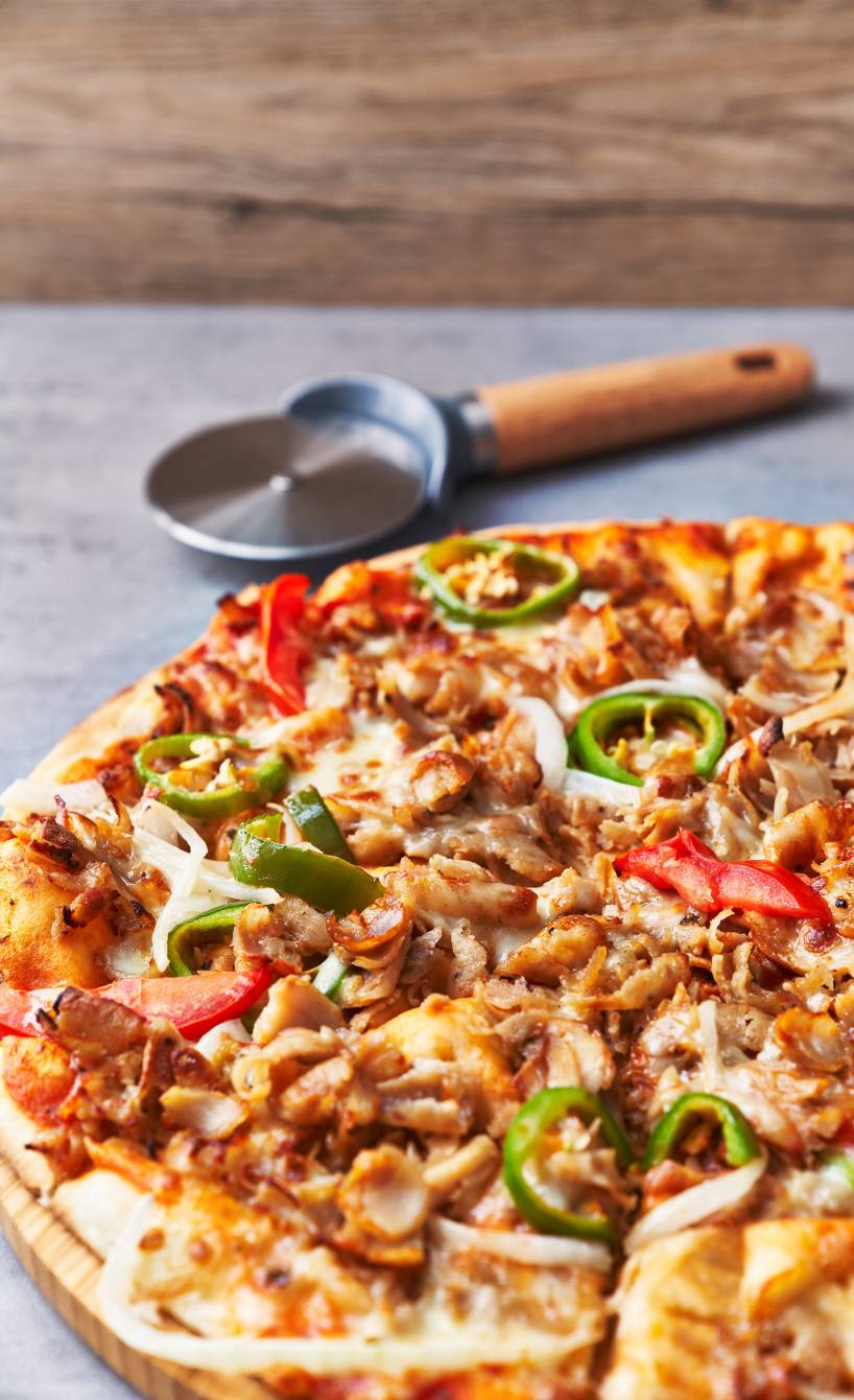 Runde Döner Pizza auf einem Pizzabrett, daneben ein Pizzaroller auf einem Tisch