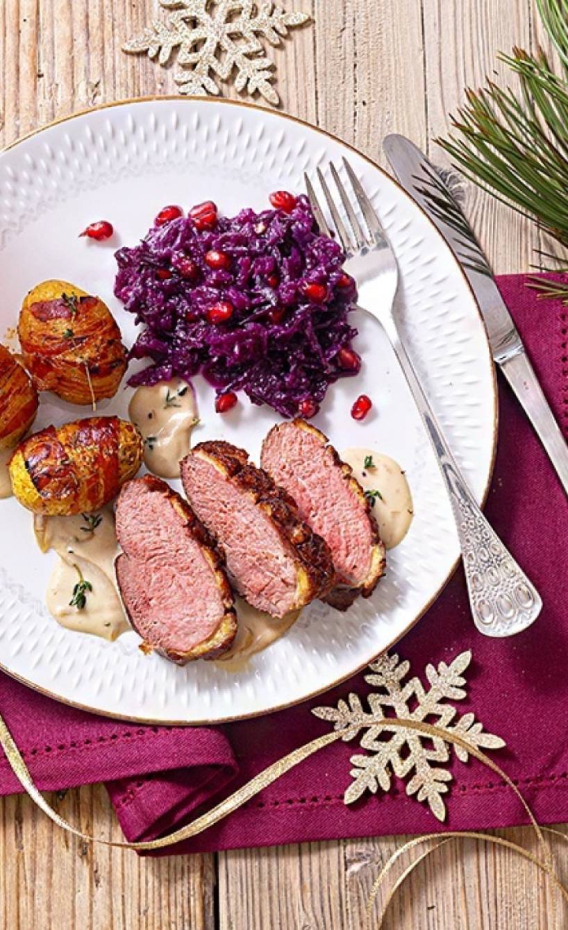 Entenbruststreifen mit Pancettakartoffeln und Rotkohl auf einem Teller, daneben Weihnachtsdeko