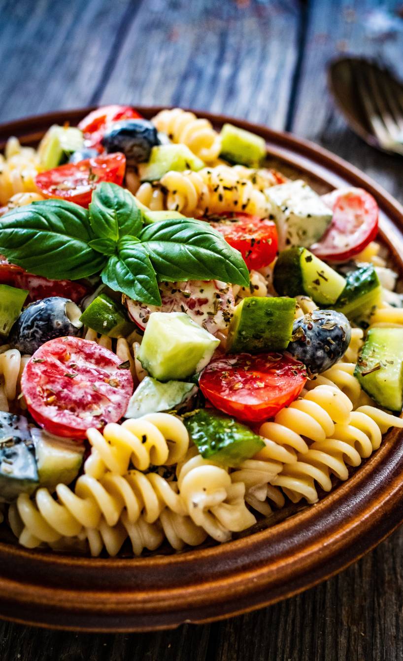 Pastasalat ohne Mayonnaise in einer Salatschüssel getoppt mit Basilikum und italienischen Kräutern