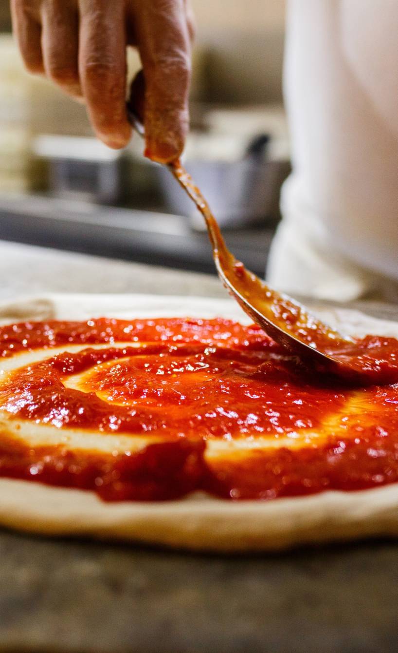 Runder Pizzateig für Pizza Napoletana wird mit Tomatensauce bestrichen