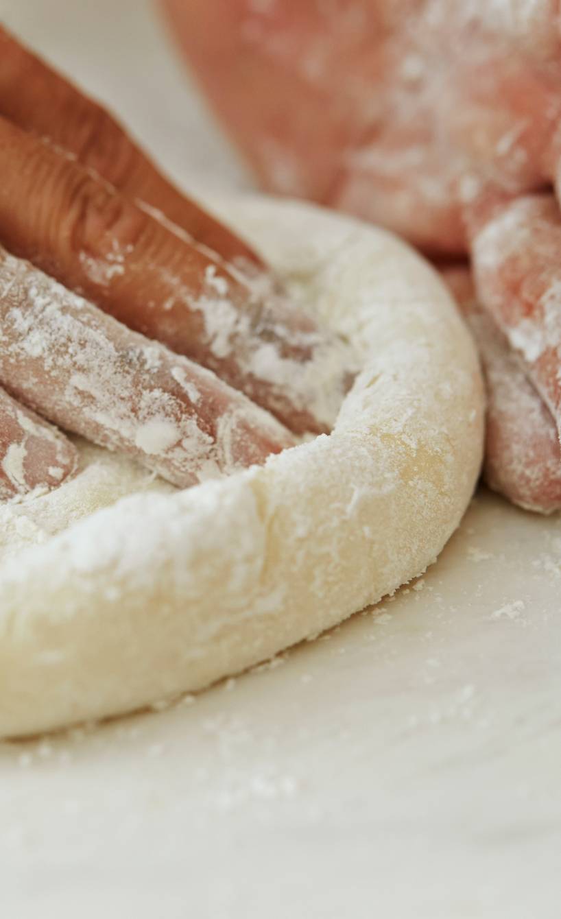 Zwei Hände formen eine runde Pizza mit hohem Rand