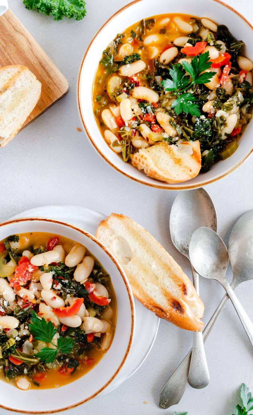 Ribollita Gemüsesuppe verteilt auf zwei Suppenteller, daneben geröstetes Ciabatta