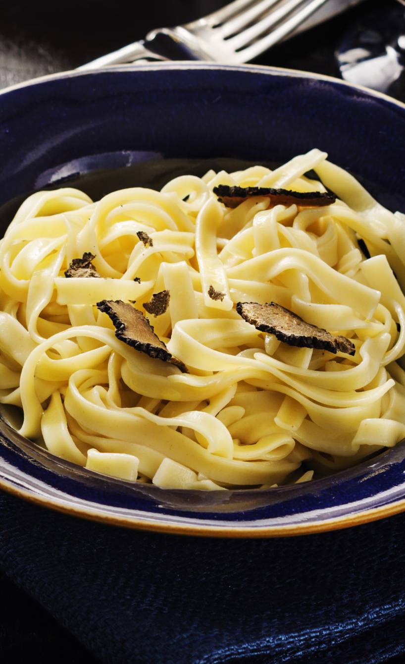 Tagliatelle al Tartufo in einem tiefen Teller, daneben eine Schale Parmesan