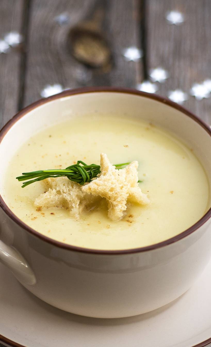 Weihnachtssuppe in einer Suppentasse getoppt mit Sternen aus Brot und Schnittlauch auf einem festlichen Tisch