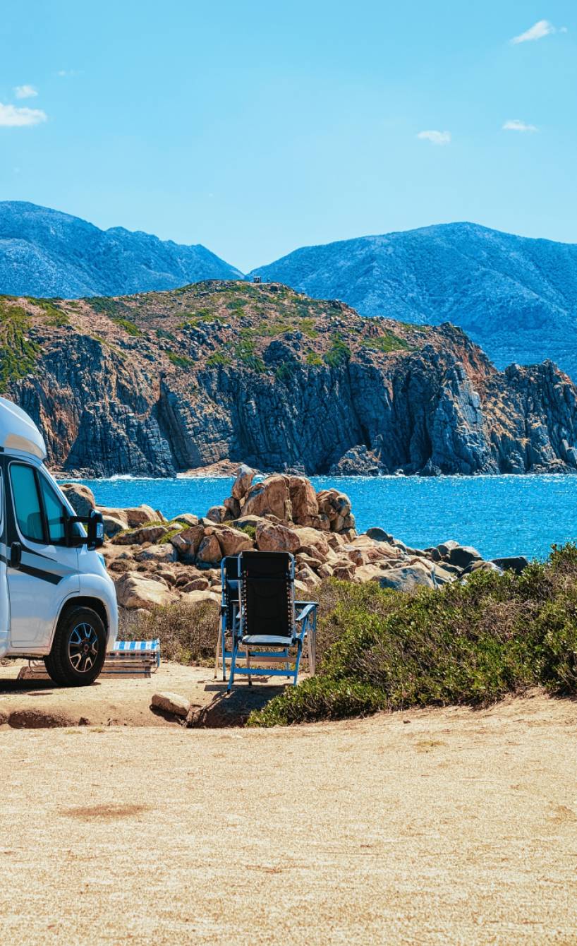Wohnmobil und Liegestuhl vor einem Strand auf Sardinien