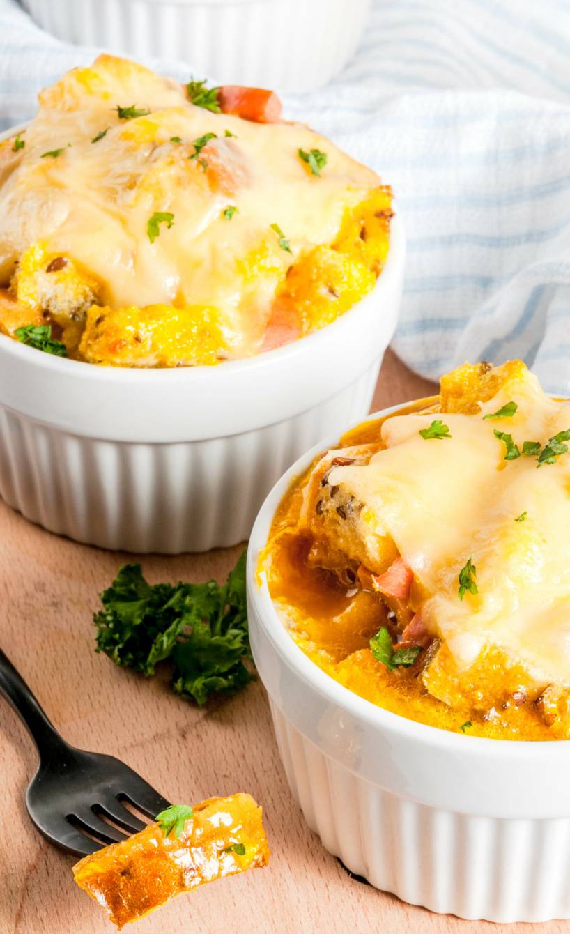 Zuppa Gallurese Brotauflauf in zwei runden Auflaufformen mit Käse überbacken auf einem Holztisch