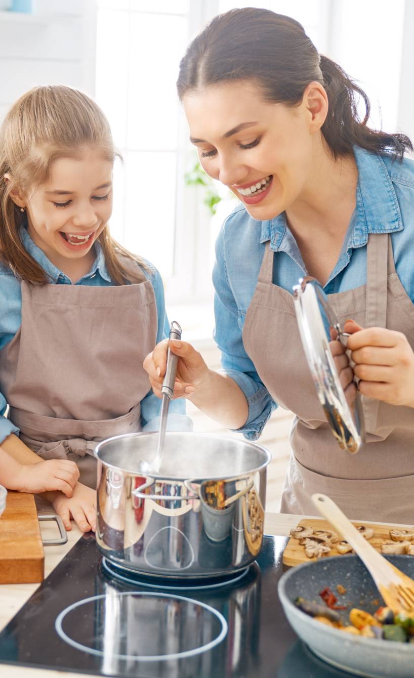 Mutter in der Küche mit zwei Kindern beim Kochen eines Gemüsegerichts und Pasta