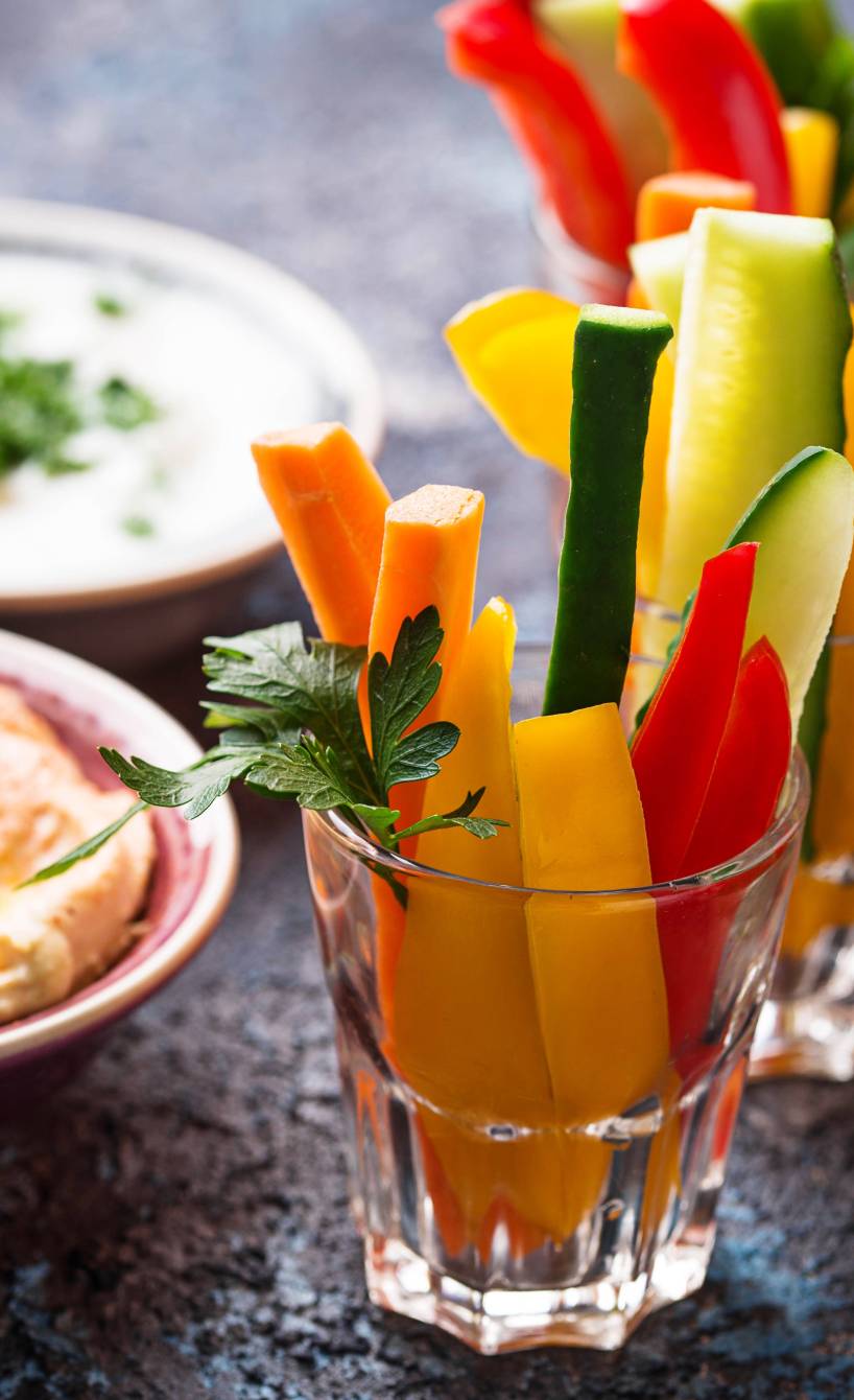 Gemüsesticks in zwei Gläsern, daneben eine Schale mit Dip