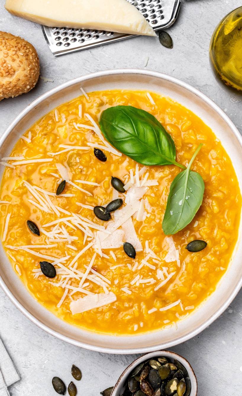 Risotto alla milanese in einem Teller, daneben Zutaten wie Parmesan und Olivenöl