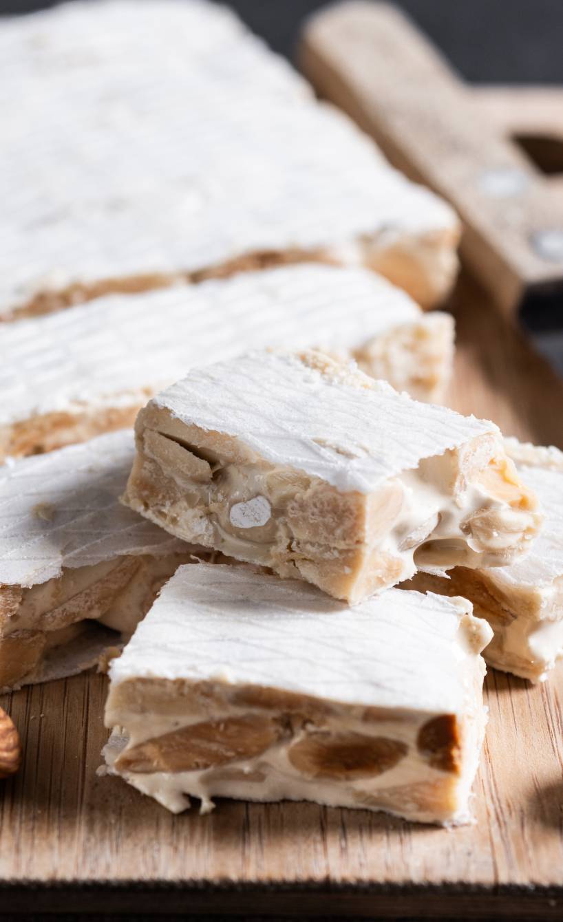 Rechteckiger Torrone angeschnitten auf einem Holzbrett, daneben ganze Mandeln