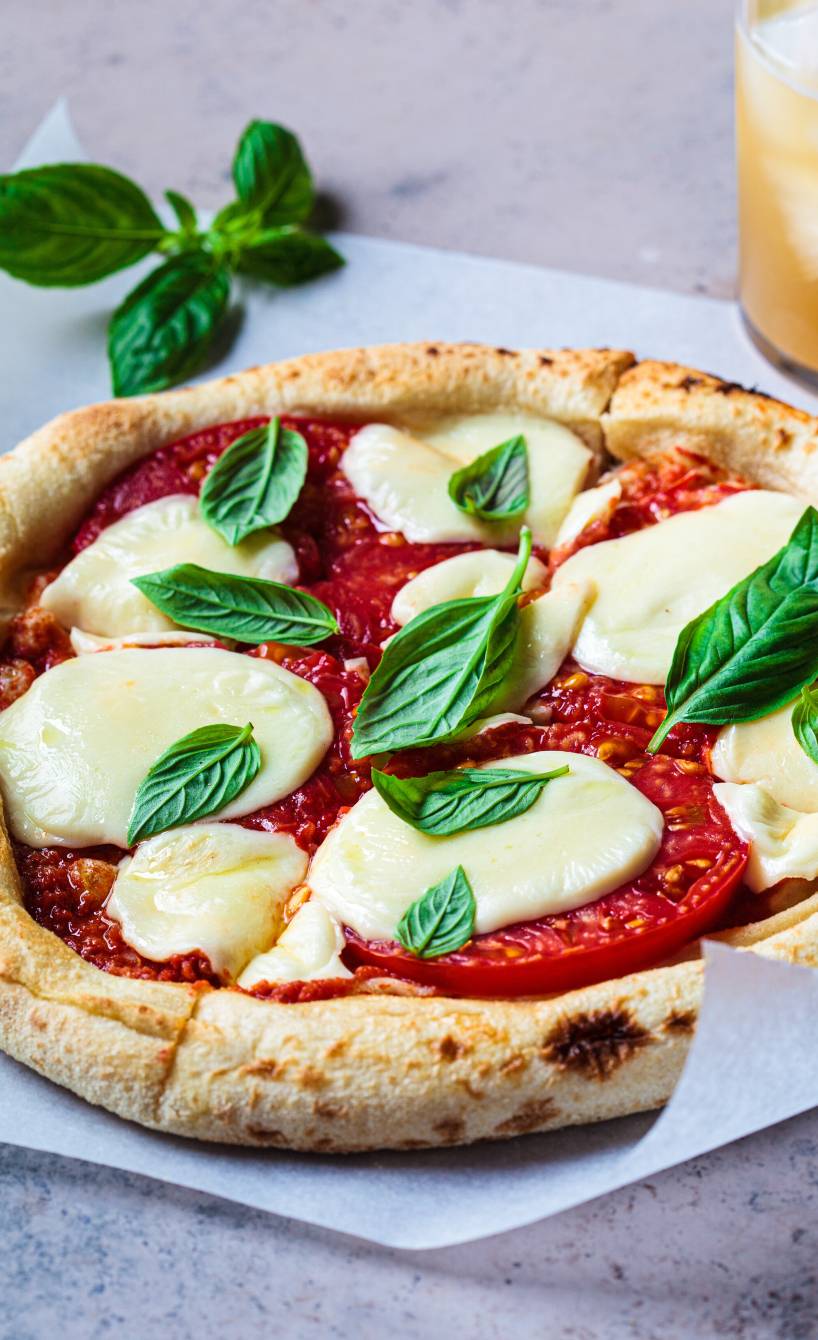 Runde vegane Pizza in Slices geschnitten auf einem Stück Backpapier garniert mit frischem Basilkum