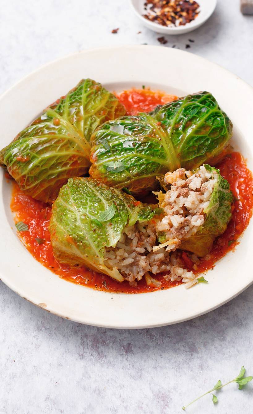 Vegane Wirsingrouladen in Tomatensauce auf einem Teller, daneben frische Kräuter