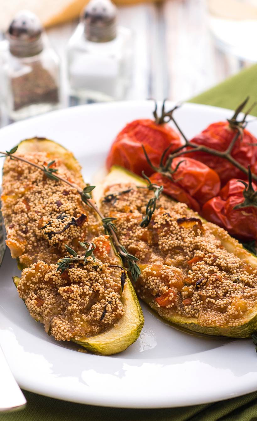 Vegane Zucchinischiffchen mit Amaranthfüllung auf einem Teller getoppt mit italienischen Kräutern