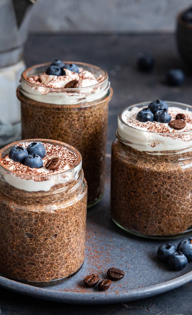 Veganer Chiapudding mit Espresso in drei Weckgläsern auf einem Tablett dekoriert mir Blaubeeren und Espressobohnen