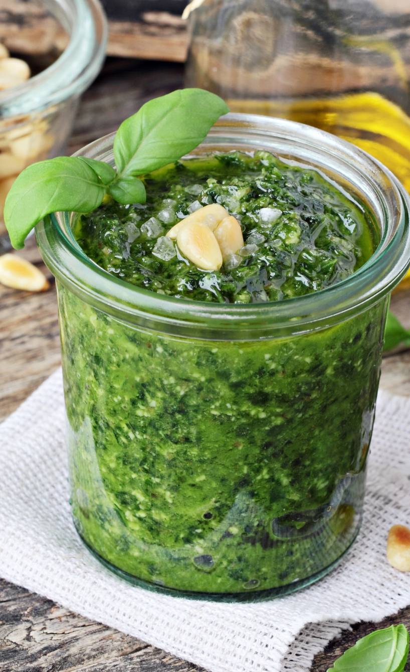 Veganes Basilikumpesto in einem Weckglas auf einem Holztisch, daneben Pinienkerne