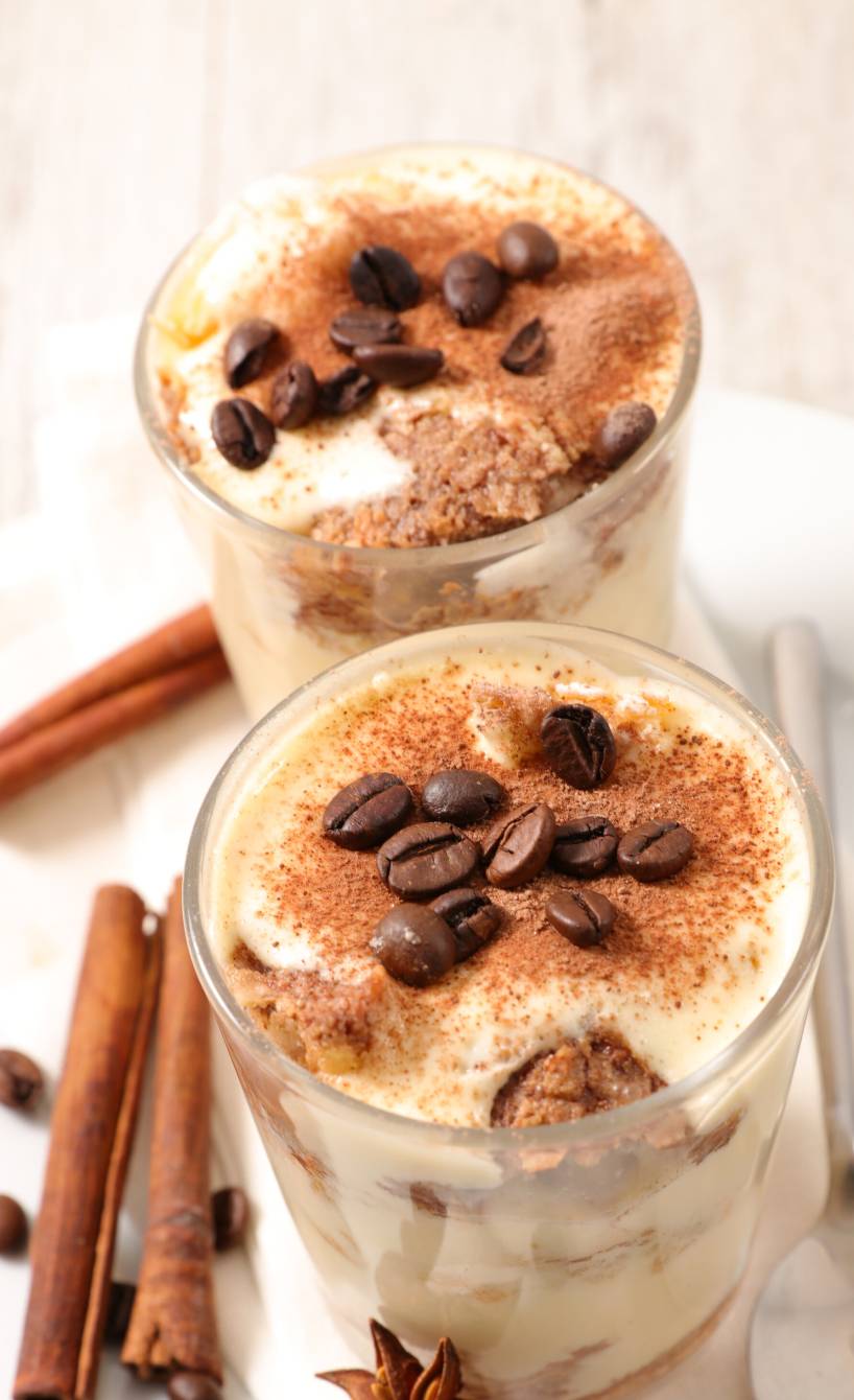 Veganes Weihnachtstiramisu in zwei Dessertgläsern dekoriert mit Zimtstangen und Sternanis auf einem Tisch