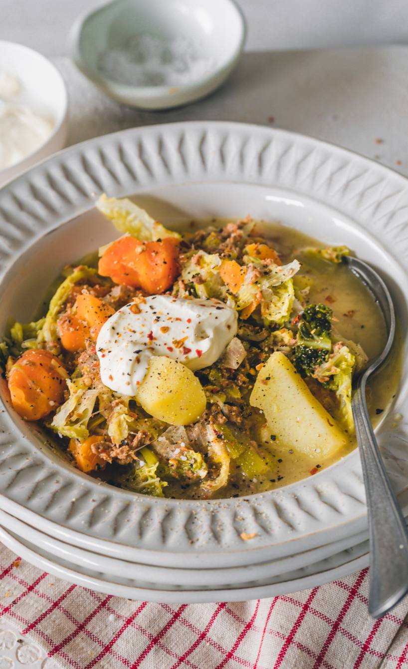 Wirsingeintopf mit veganem Hackfleisch in einem Suppenteller getoppt mit veganer Crème fraîche