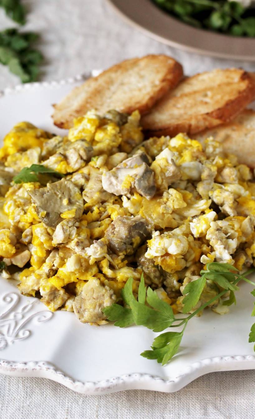 Agnello Cacio e Uova Rührei mit Lamm und Käse auf einem weißen Teller, daneben geröstete Brotscheiben