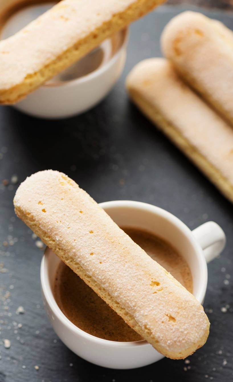 Selbst gebackene Löffelbiskuits auf einer Schieferplatte mit einer Tasse Espresso
