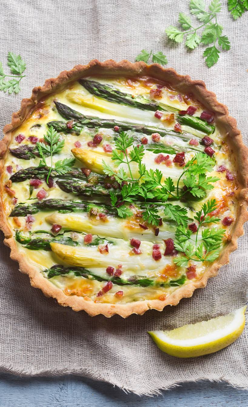 Runde Spargelquiche mit weißem und grünem Spargel mit Schinkenwürfeln auf einem frühlingshaft dekorierten Tisch