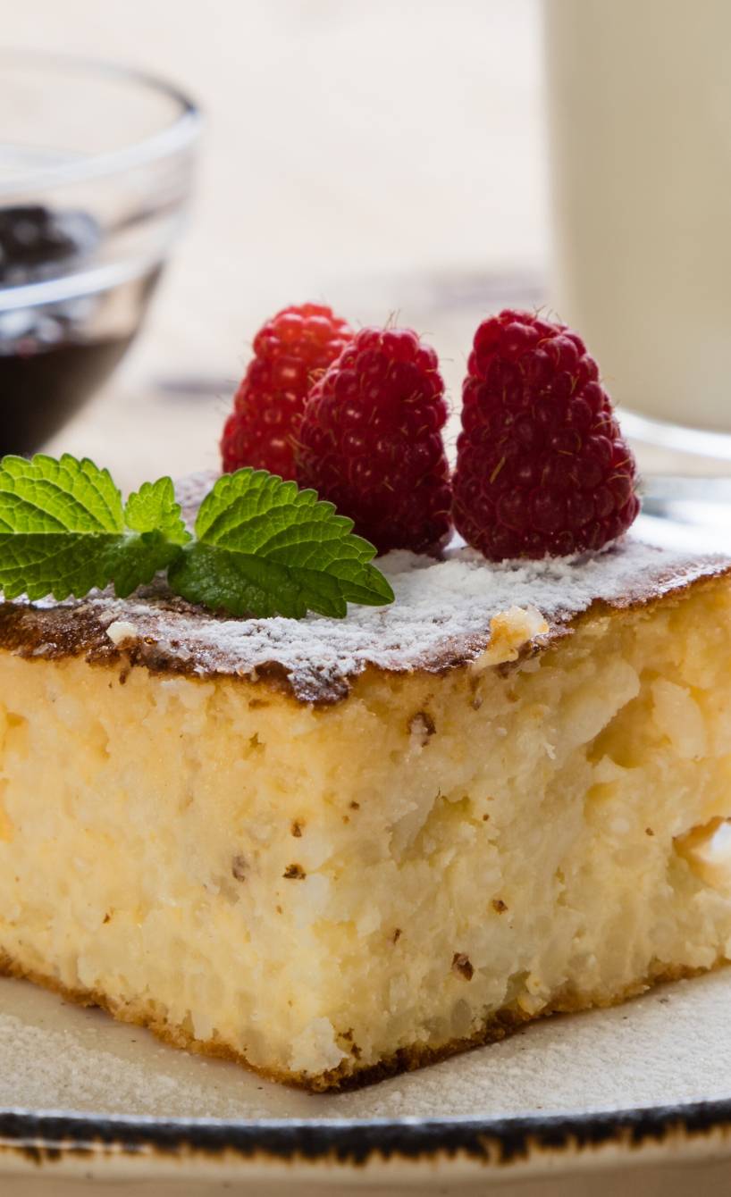 Ein Stück Torta di Riso Reiskuchen auf einem Kuchenteller bestäubt mit Puderzucker und dekoriert mit Himbeeren und Minze