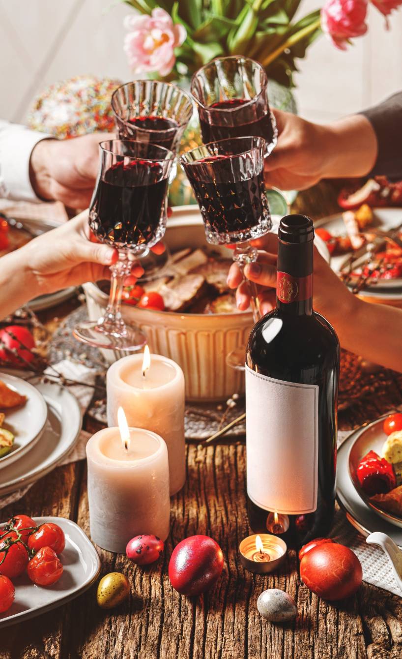 Vier Personen stoßen mit Rotwein an einem mit italienischen Ostergerichten gefüllten und dekorierten Tisch an