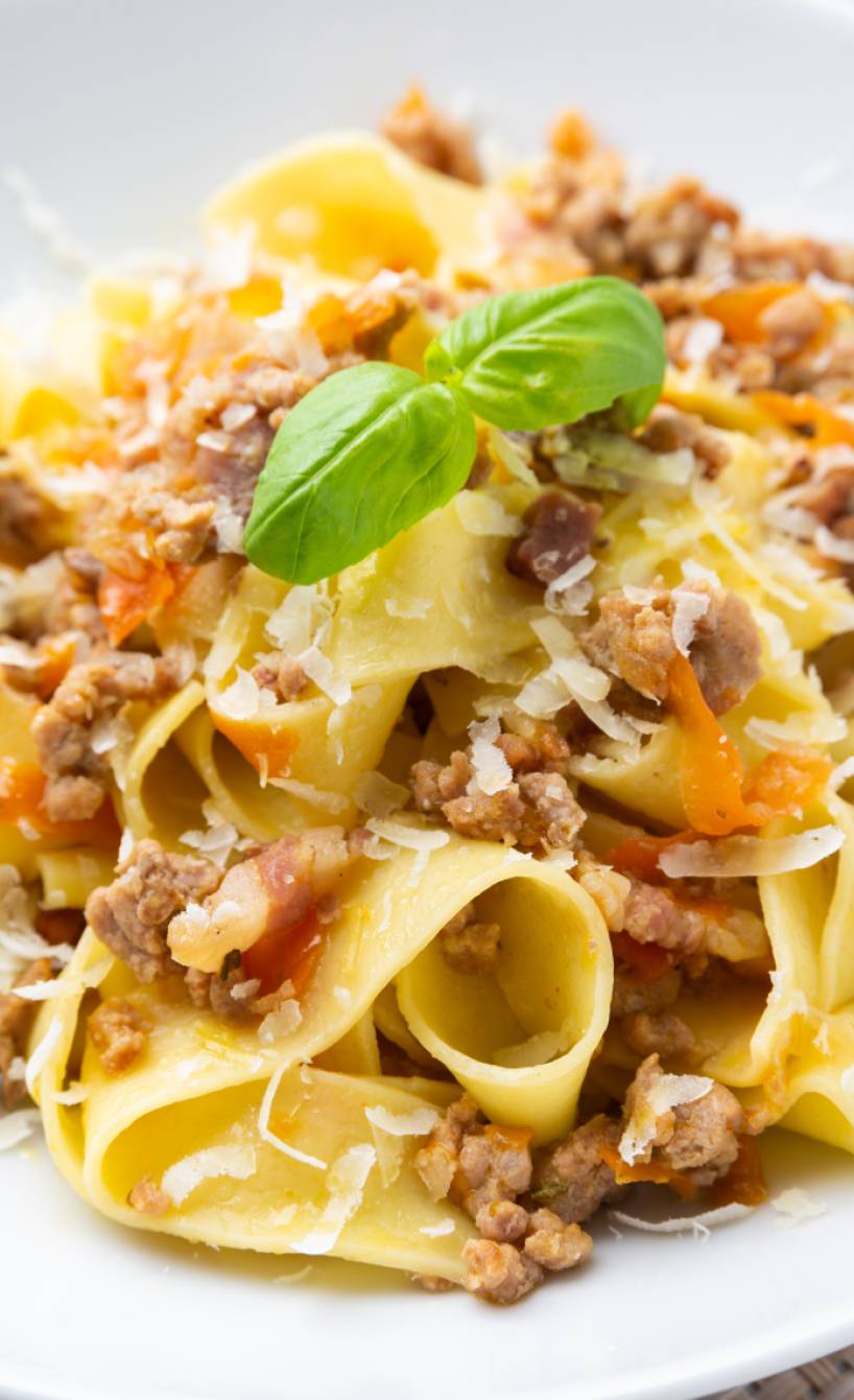 Weiße Bolognese mit Pappardelle auf einem tiefen, weißen Teller dekoriert mit frischem Basilikum