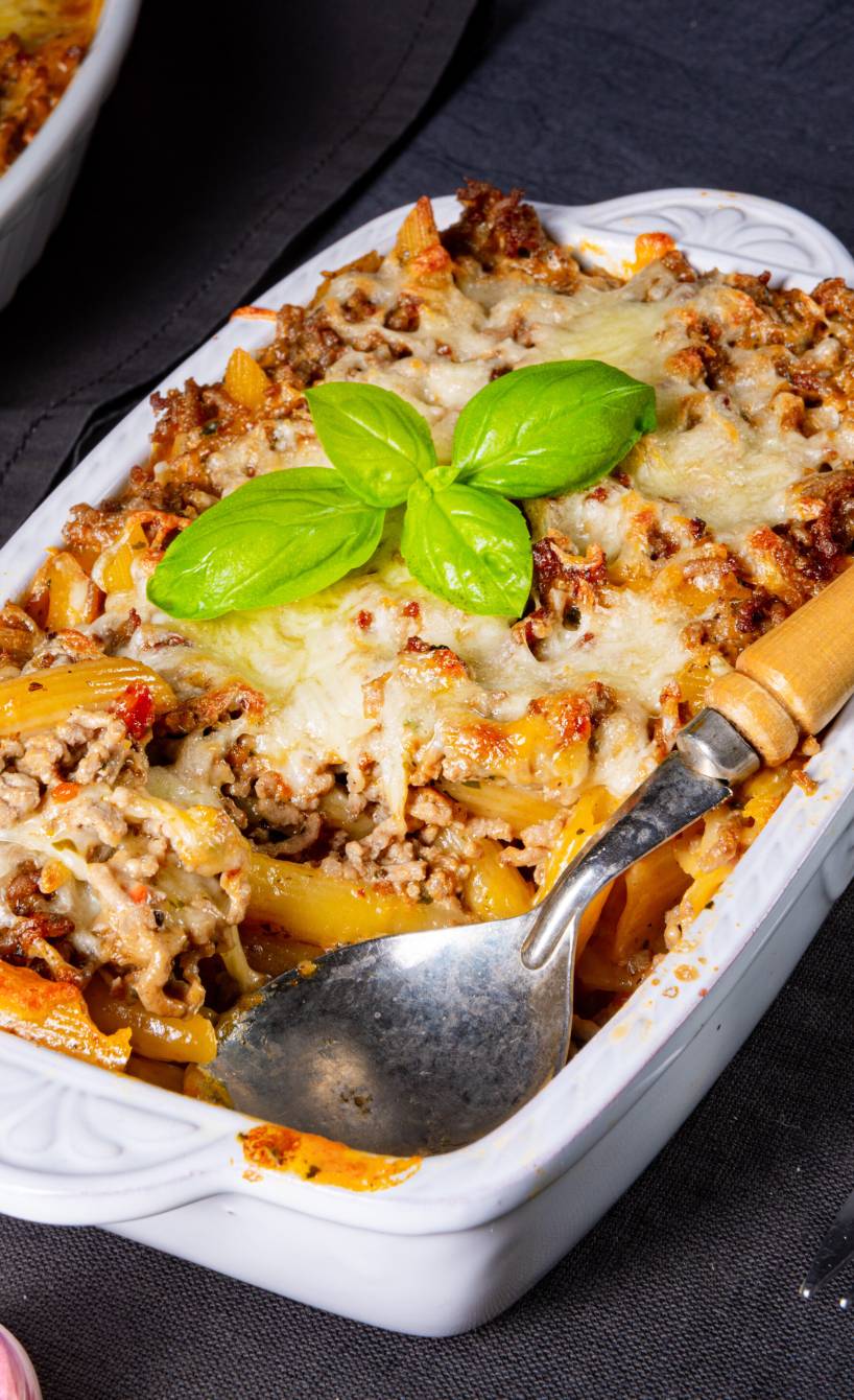Bolognese-Auflauf in einer weißen Auflaufform mit Schichten aus Hackfleischsoße und Penne mit Käse gratiniert auf einem Tisch