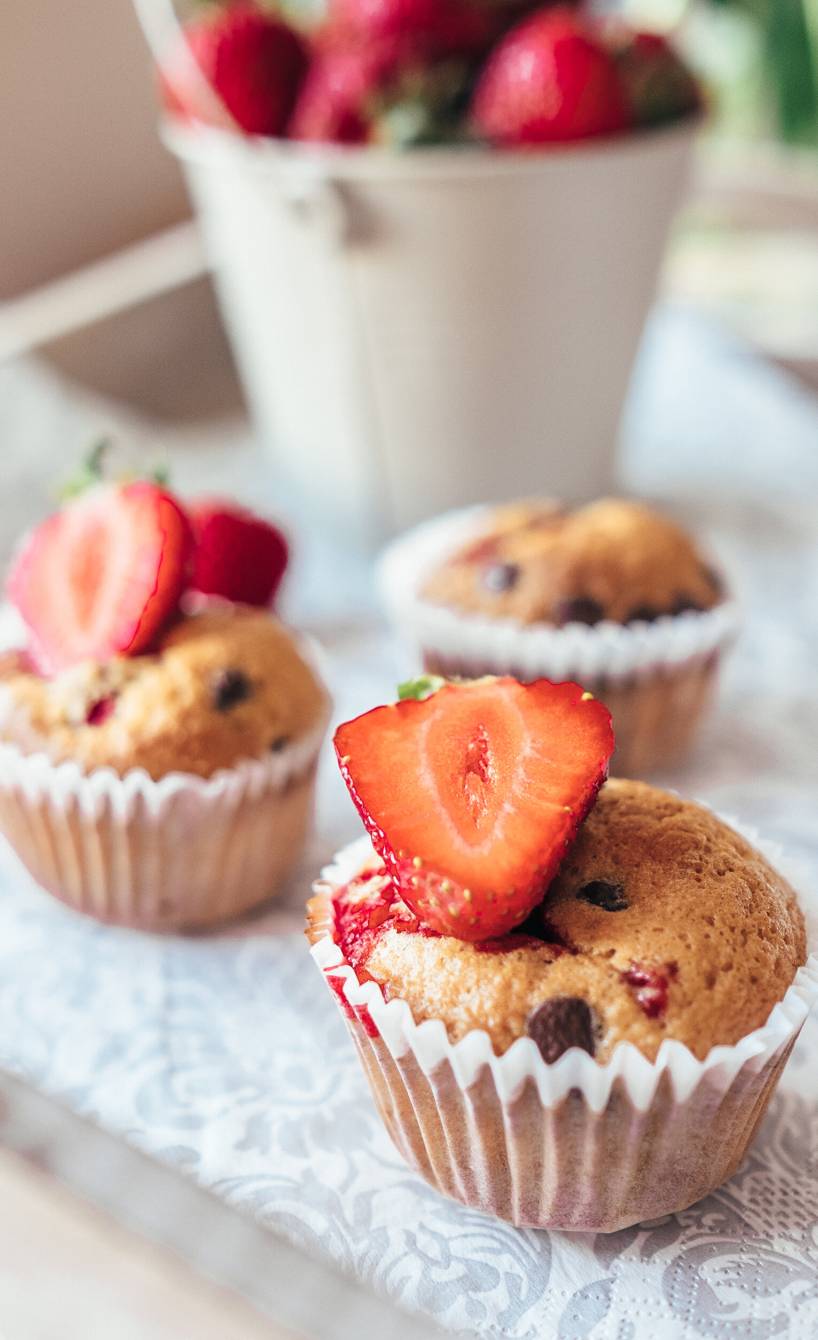 Drei Erdbeer-Muffins dekoriert mit einer halben Erdbeere auf einem Küchentisch