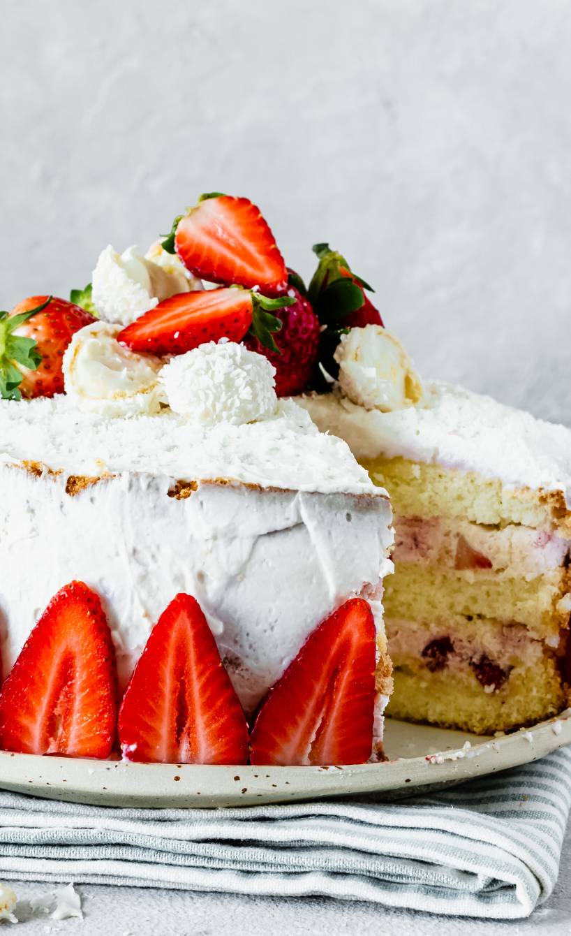 Erdbeer-Raffaello-Torte angeschnitten auf einer Tortenplatte dekoriert mit Mascarponecreme und frischen Erdbeeren