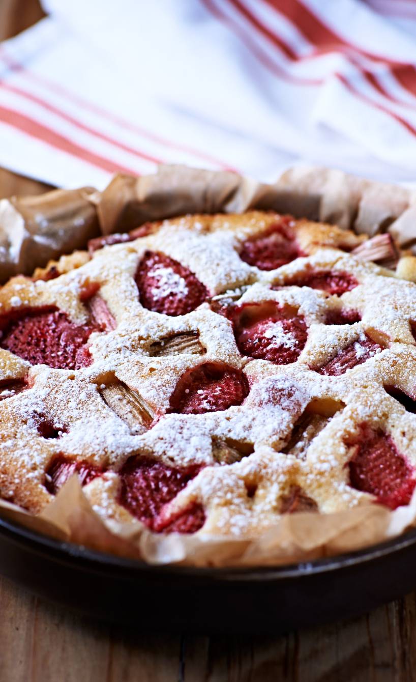 Runder Erdbeer-Rhabarber-Kuchen in einer Springform bestäubt mit Puderzucker
