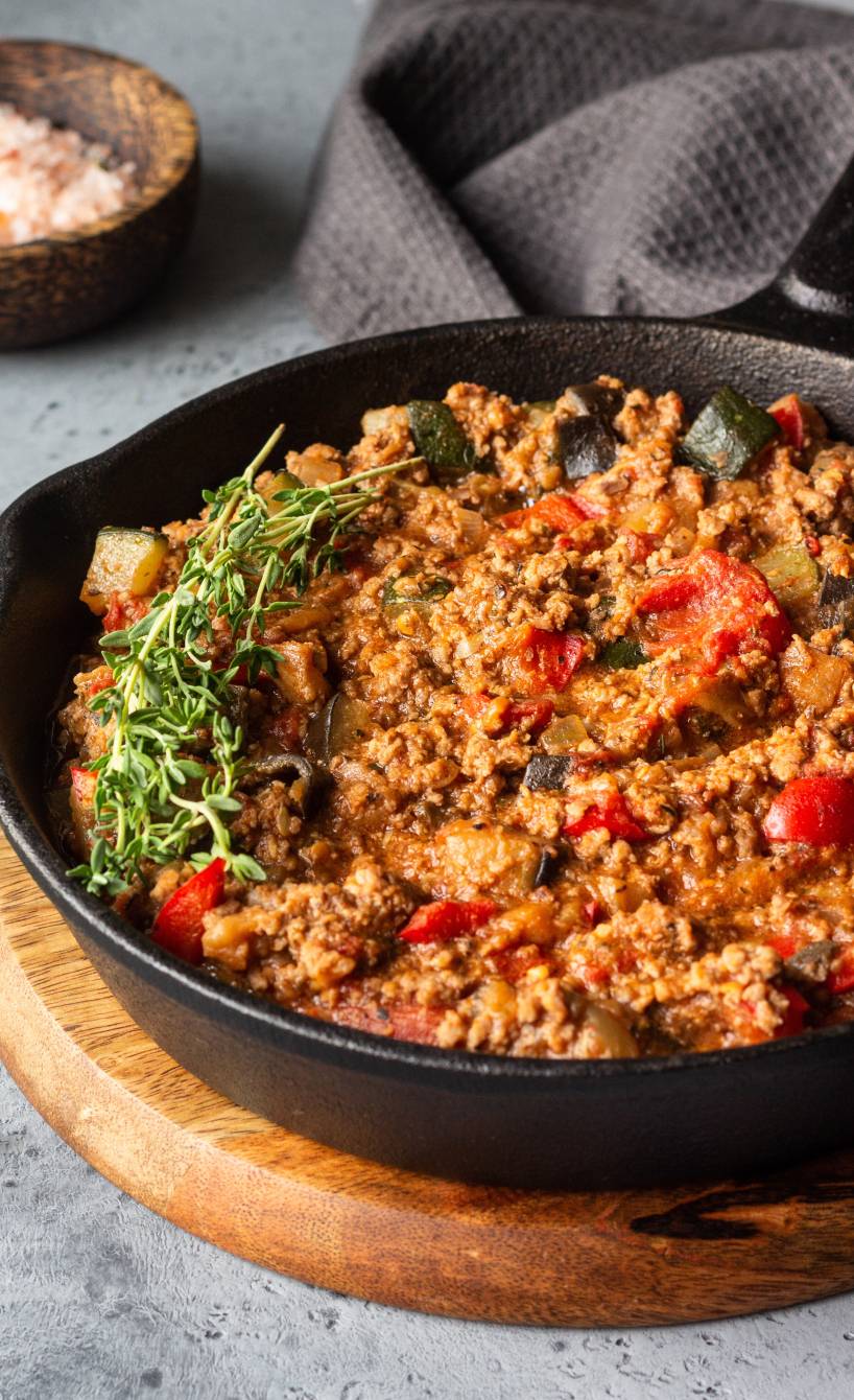 Gemüsebolognese mit Hackfleisch, Paprika, Zucchini und Oliven in einer Pfanne garniert mit frischen Kräuter