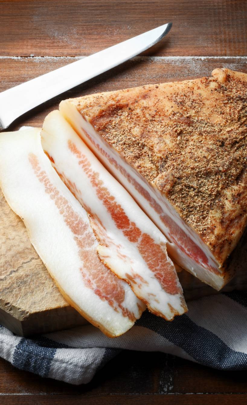 Ein ganzes Stück Guanciale italienischer Speck angeschnitten auf einem Holzbrett