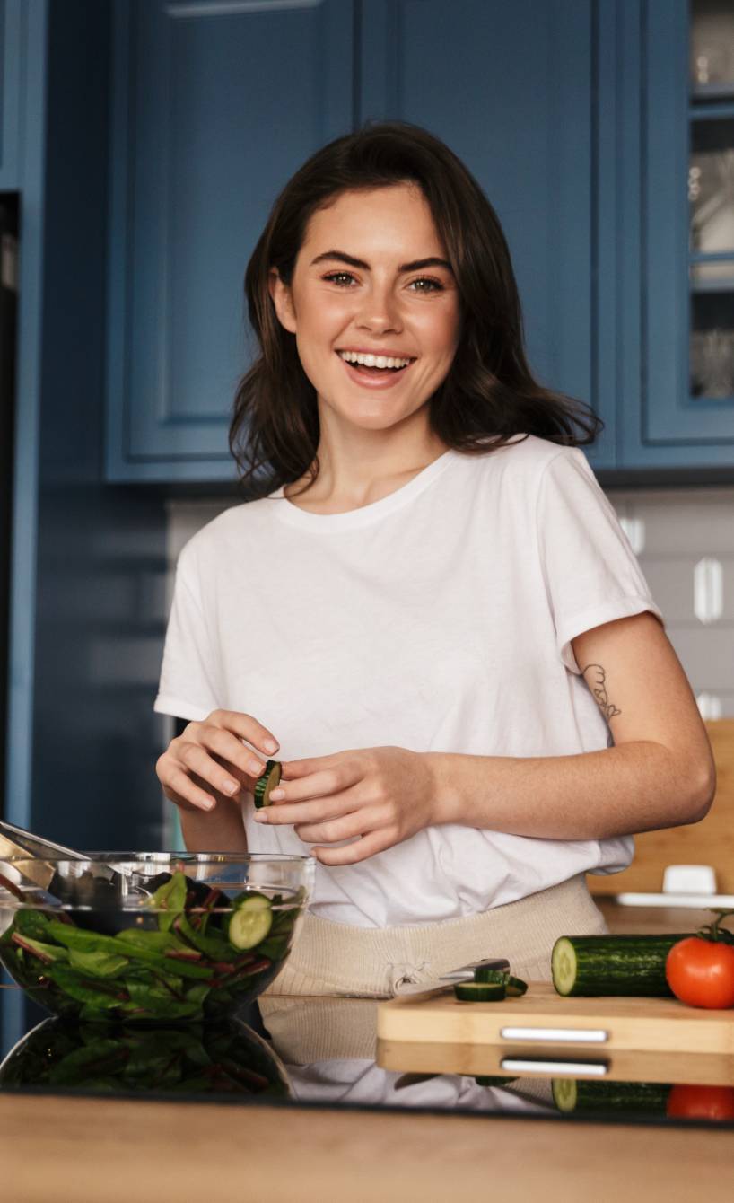 Frau mittleren Alters bereitet in ihrer Küche lächelnd einen italienischen Salat aus frischen Zutaten zu