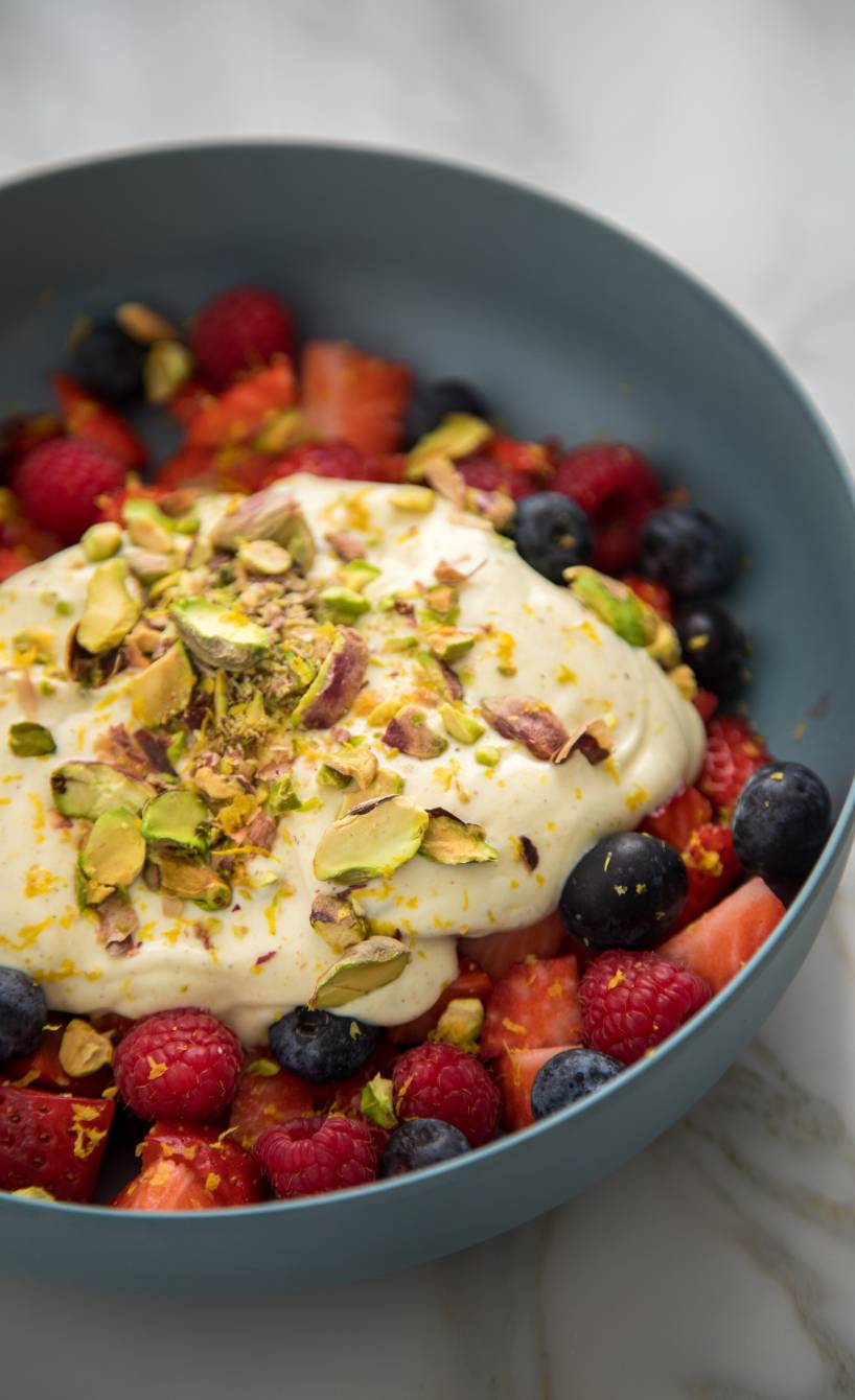 Obstsalat aus Beeren mit Leinöl-Quark-Creme in einer grauen Schale getoppt mit Zitronenabrieb und Pistazien