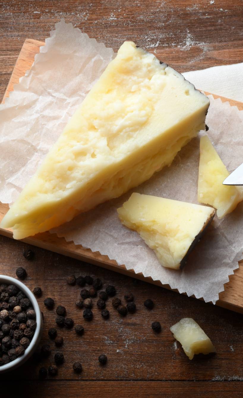 Ein großes Stück Pecorino Käse auf einem Holzbrett, einige Stücke sind abgebröckelt