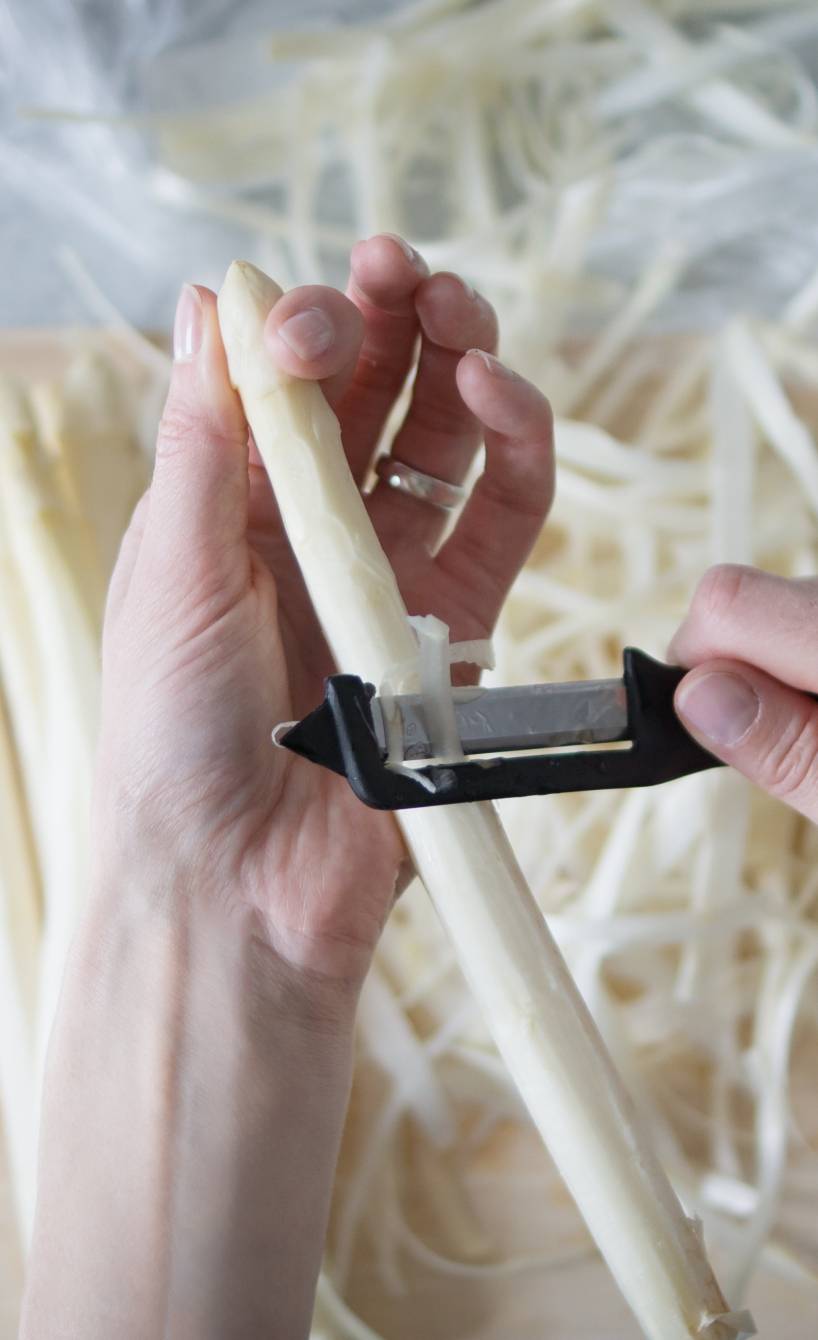 Frau schält Spargel mit einem Sparschäler über einem Holzbrett